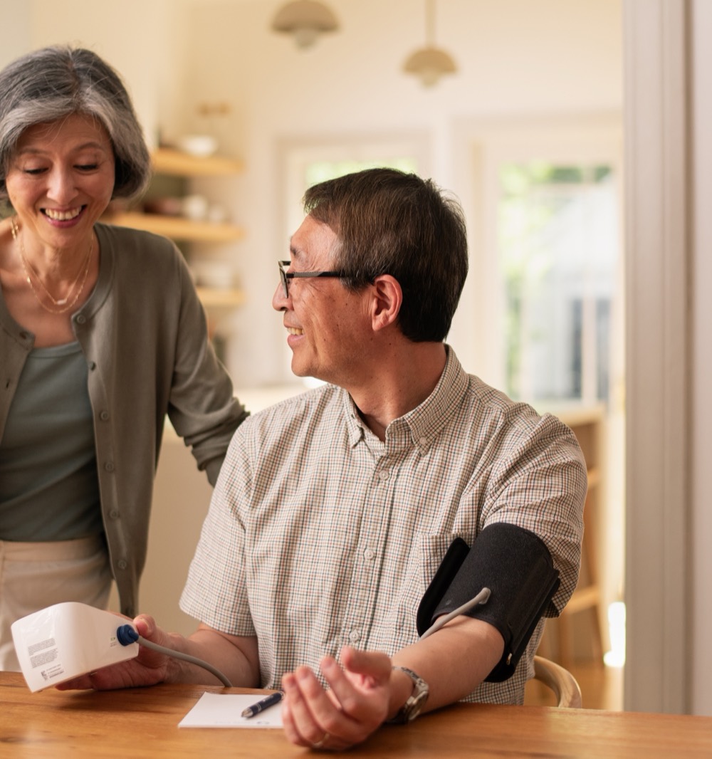 A woman helping a senior man check his blood pressure at home