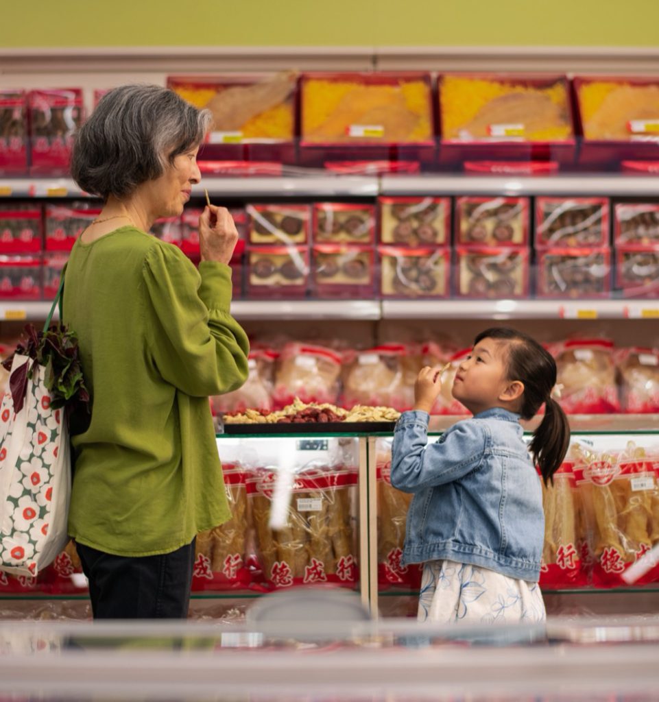 A grandmother and child shopping for groceries and herbal products at a market